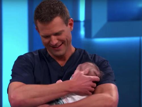 Arzt fragt, ob er das Neugeborene eines Gasts aus dem Publikum halten darf und realisiert dann, dass das Baby nicht echt ist