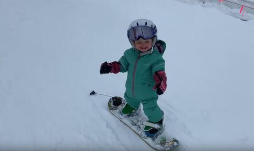 Ein 1 jähriges Mädchen hört gar nicht mehr auf zu lächeln, als sie auf ihrem winzigen Snowboard losdüst