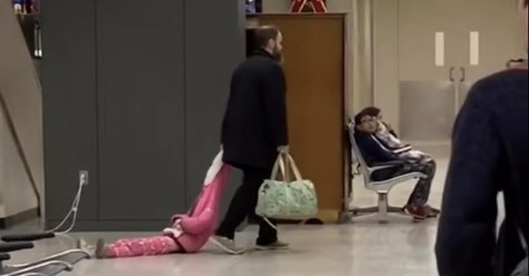 Ein frustrierter Vater zieht seine Tochter durch den Flughafen an ihrer Kapuze